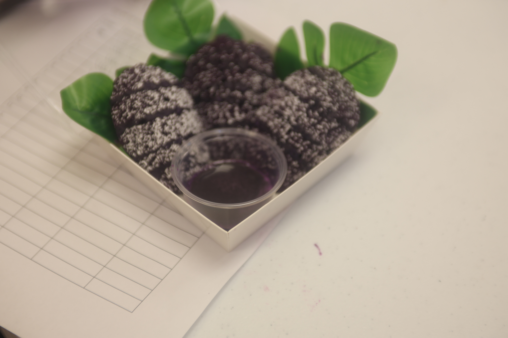 Dark ube dessert bites dusted with sugar, served with a purple sauce.