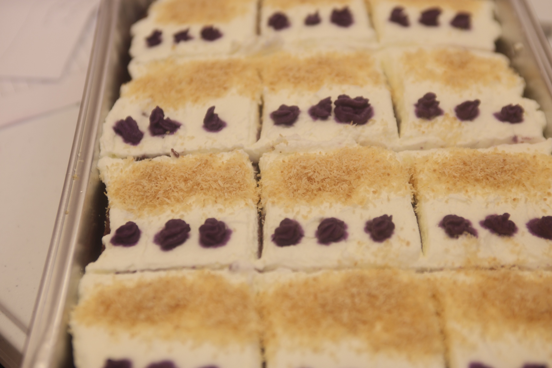 Tray of ube and coconut squares topped with toasted coconut and purple piping.