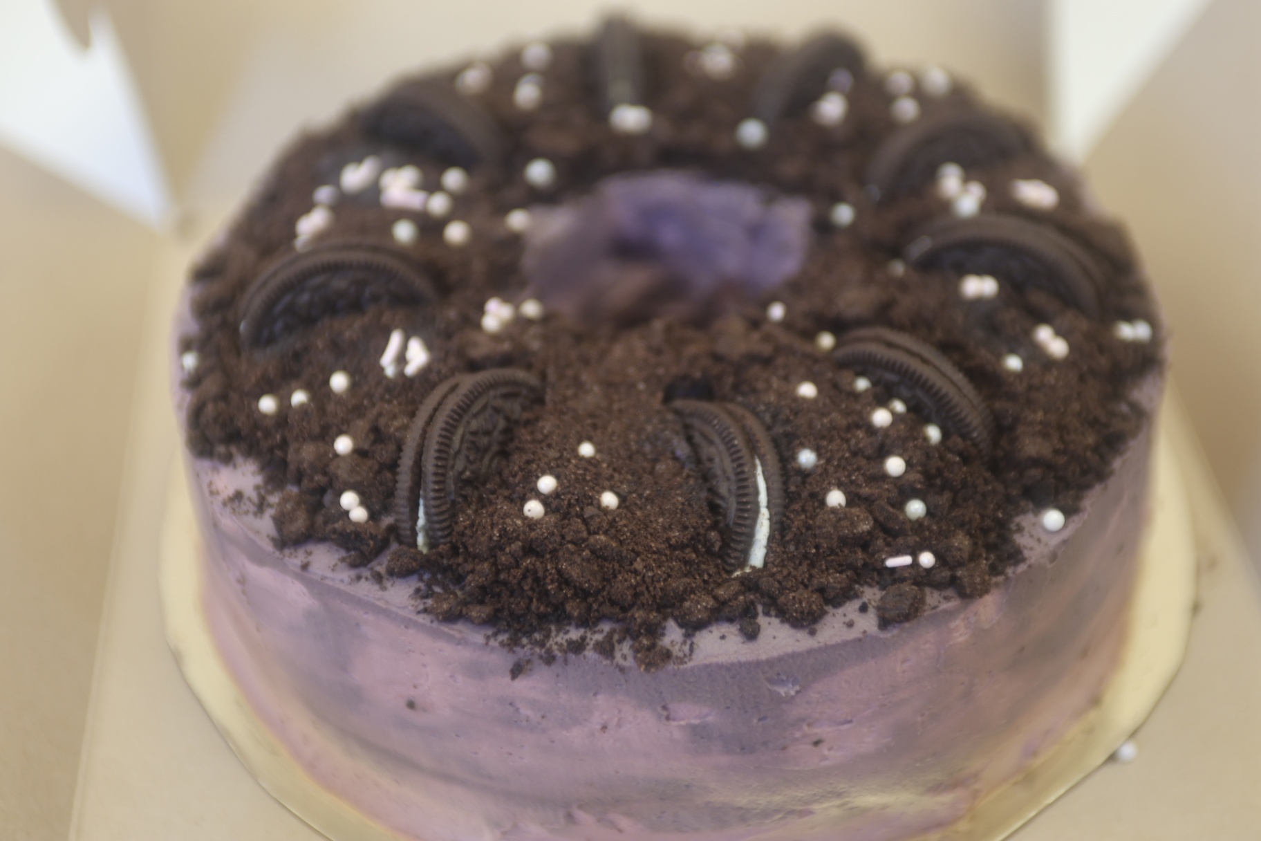 Ube dessert cake topped with chocolate cookie crumble, Oreo halves, and pearl sprinkles.