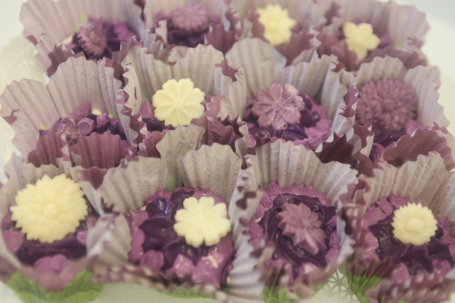Ube dessert bites presented in cupcake liners with purple and white floral toppings.